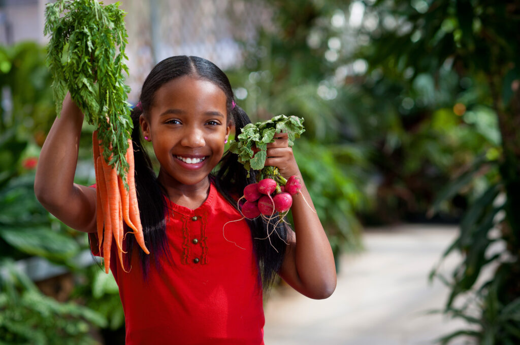 photo of girl holding carrots and radishes