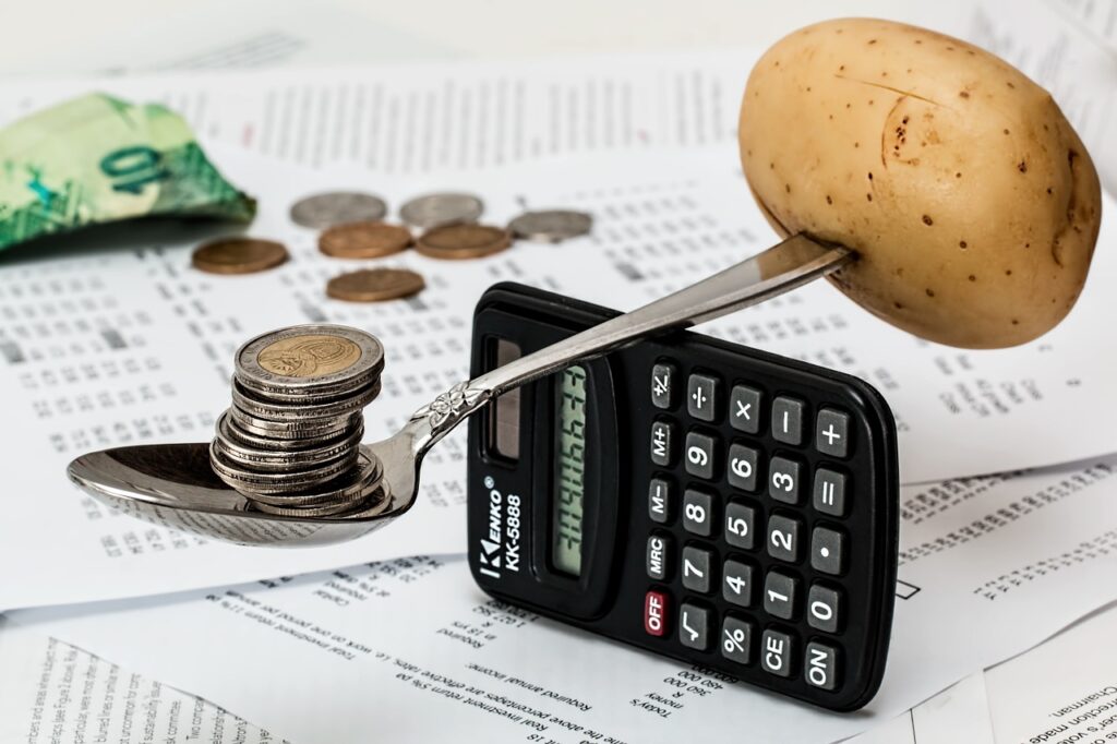Spoon with a potato on one end and coins on the other, balancing on a calculator.